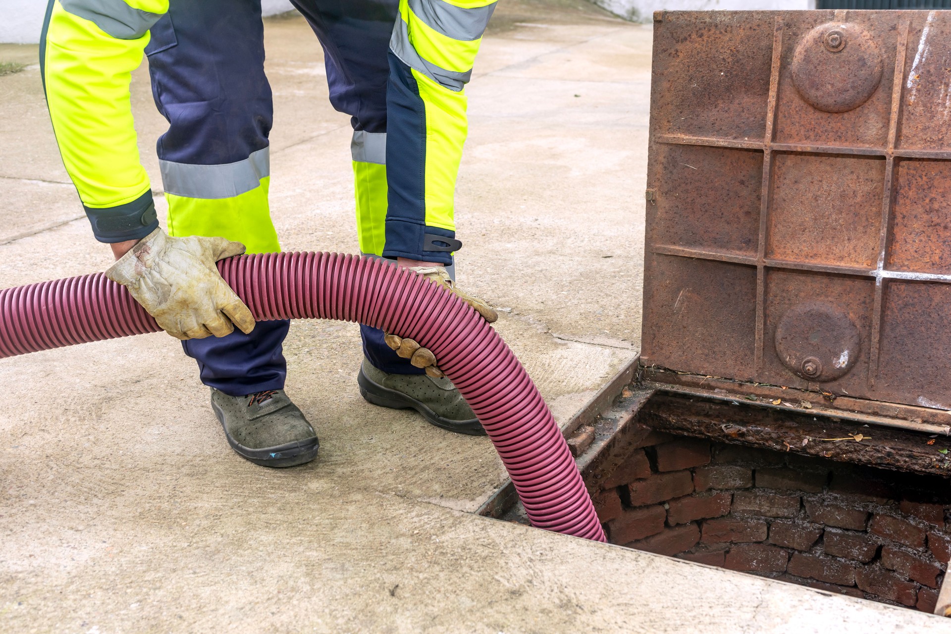 Sewer worker cleaning, unclogging and draining sewage manhole.